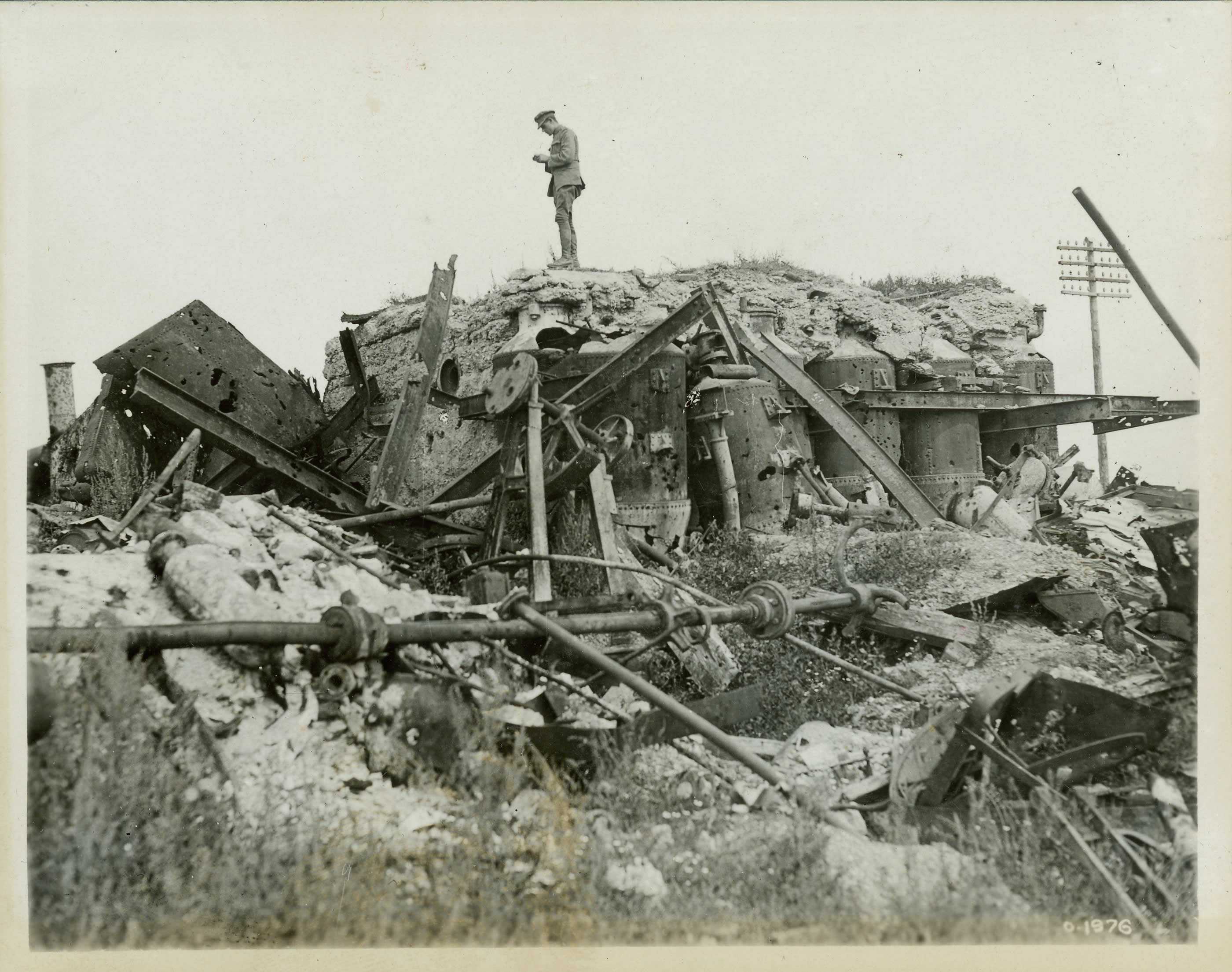 Black and white photograph. A lone soldier stands on the ruins of a sugar factory. Various mechanical implements are visible in the rubble.